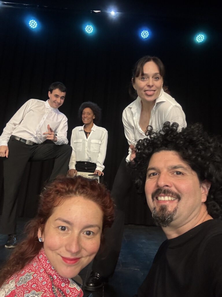 Grupo diverso de personas en un escenario teatral, compartiendo un momento de complicidad y juego escénico.
La imagen transmite el teatro como espacio de encuentro, creación colectiva y exploración de realidades sociales.